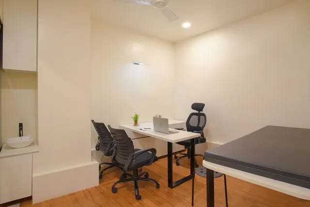 A consultation room with a desk, visitor chairs and an examination bed.