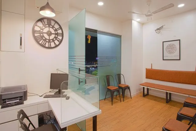 Clinic waiting area with chairs, a wall clock and a glass partition.