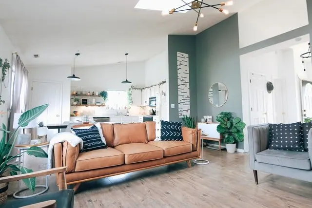 An open living room with a tan sofa, patterned seating and indoor plants.