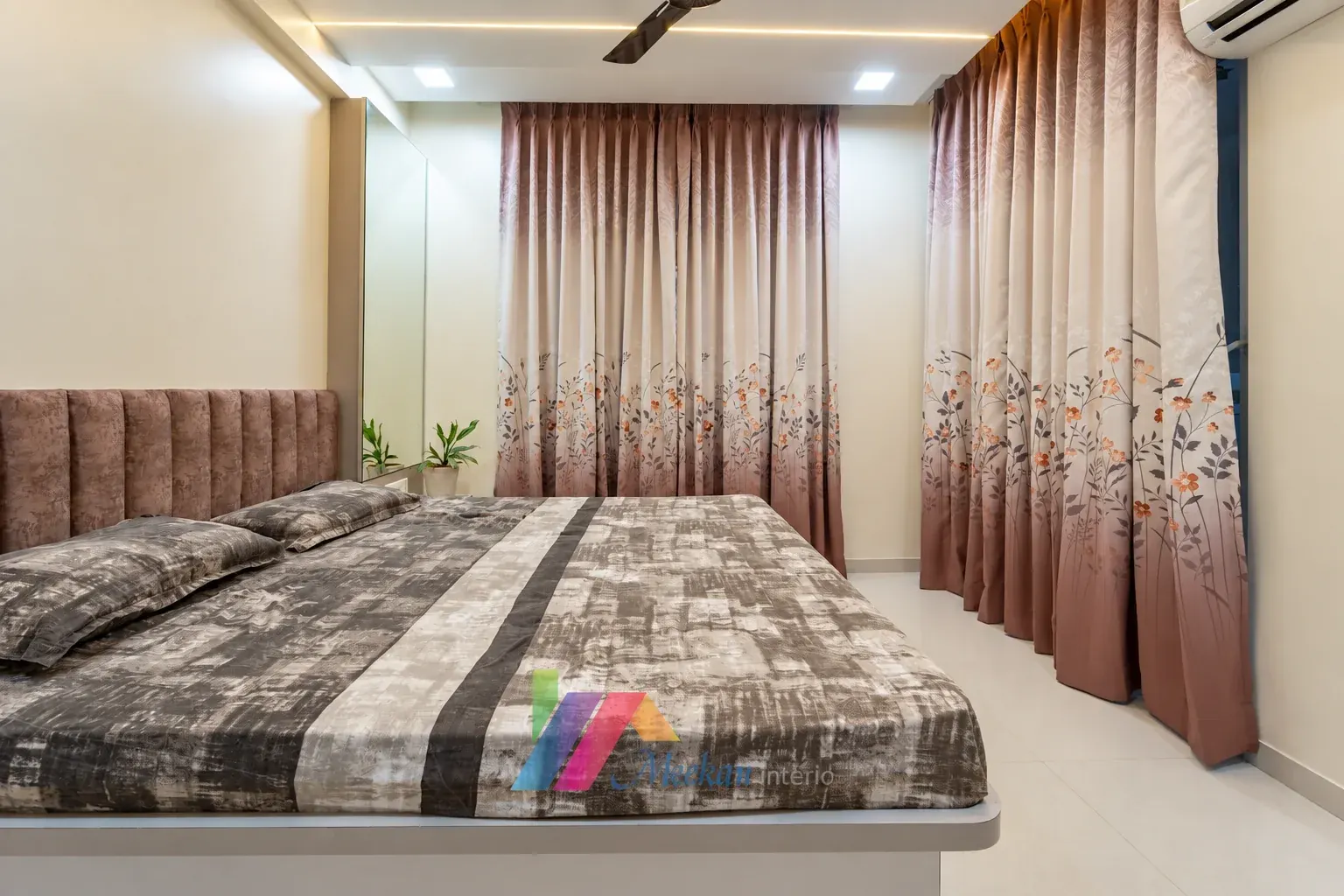 Bedroom with a padded headboard, patterned bedspread and floral curtains.