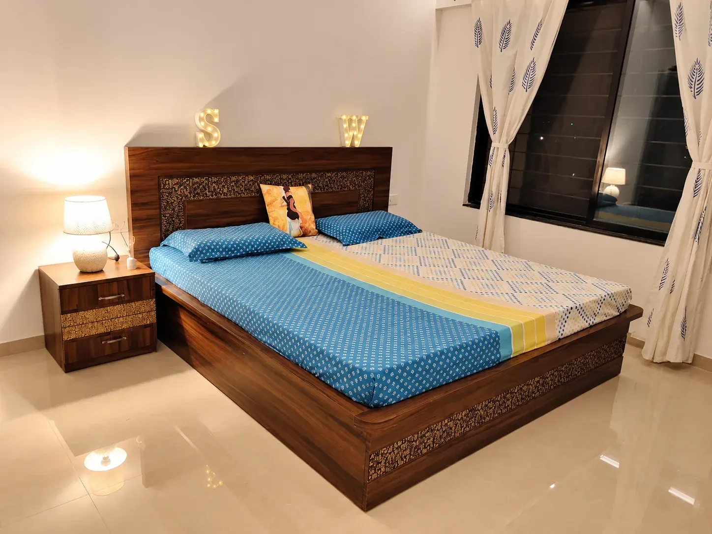 Bedroom with a timber bed, blue bedding and a bedside lamp.