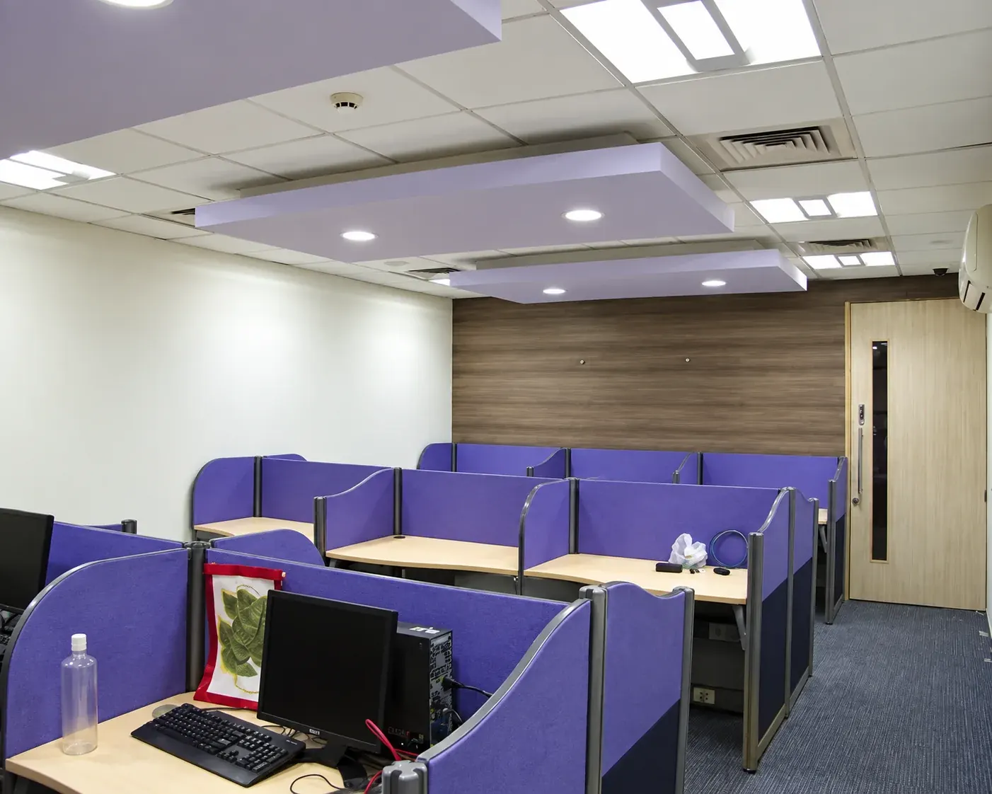 Office interior with purple workstations beneath a suspended ceiling.