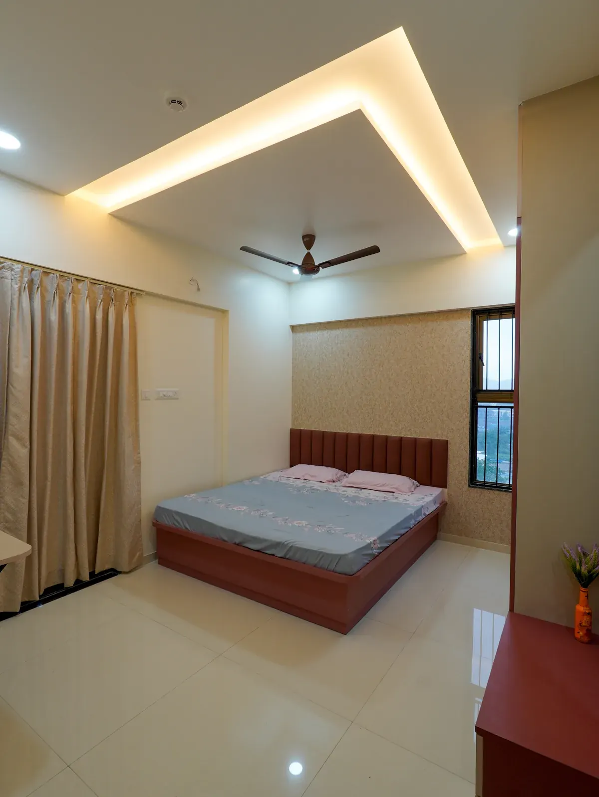 A bedroom with a timber bed, full-height curtains and warm concealed ceiling lighting.