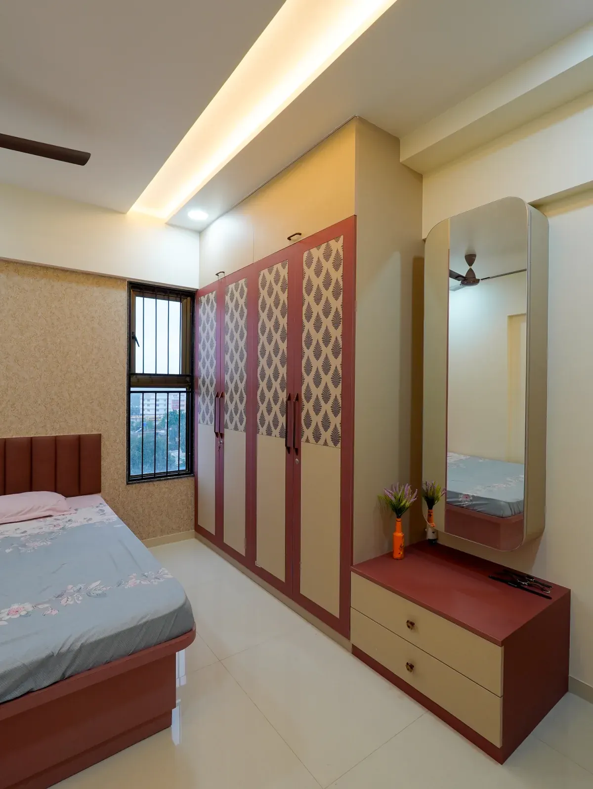 A wardrobe and dressing area with patterned panels, a tall mirror and a low drawer unit.