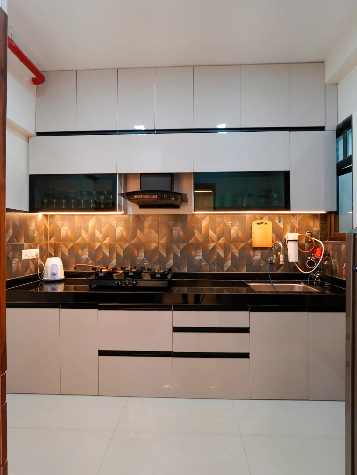 A kitchen with pale cabinetry, dark worktops and an illuminated geometric backsplash.